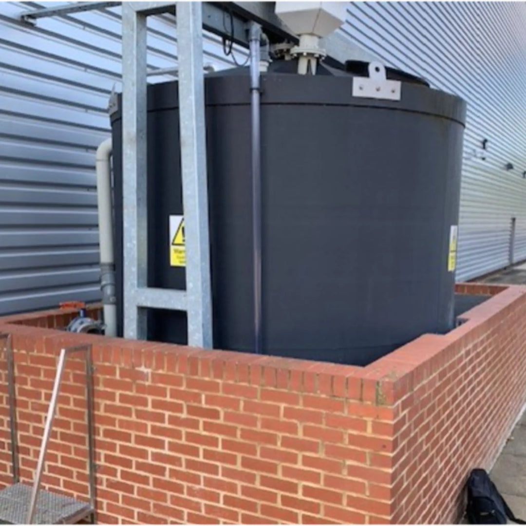 Large black cylindrical tank on a brick platform with a building in the background