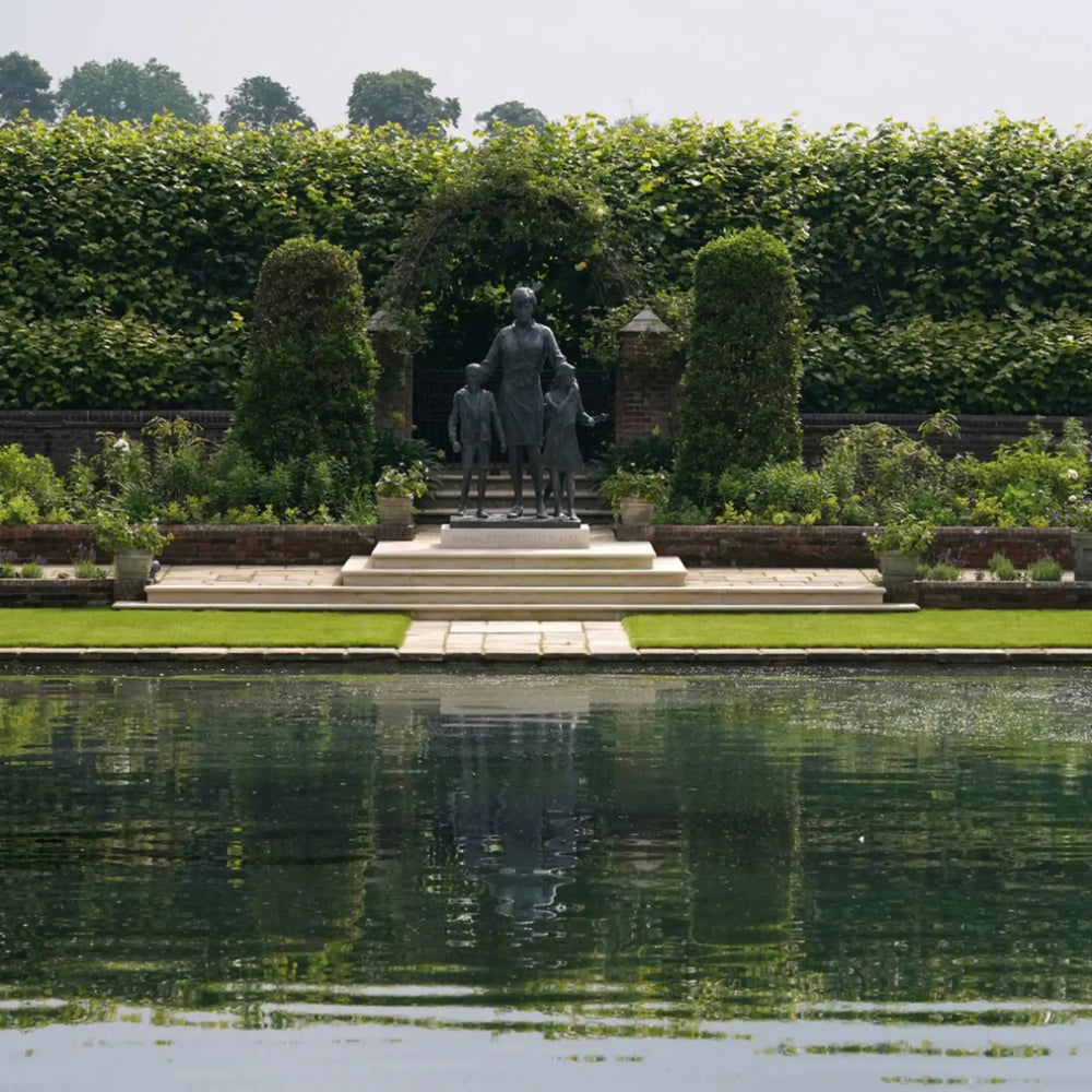 Statue of a man with two children in a garden setting with a pond.
