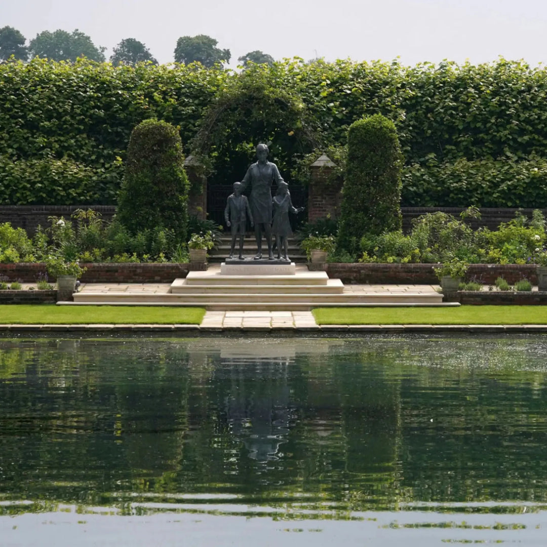 Statue of a man with two children in a garden setting with a pond.