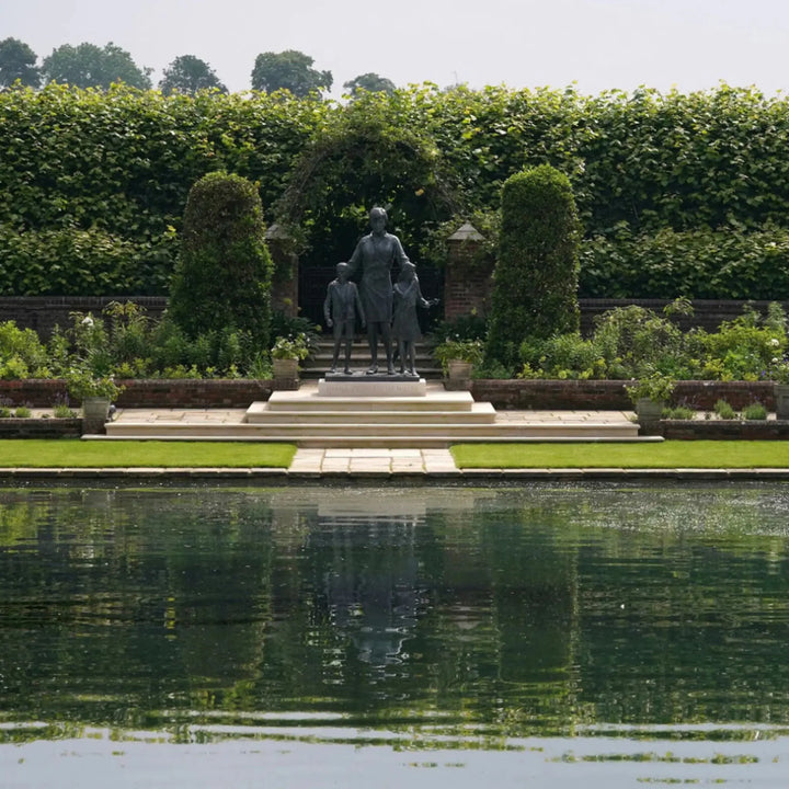 Statue of a man with two children in a garden setting with a pond.