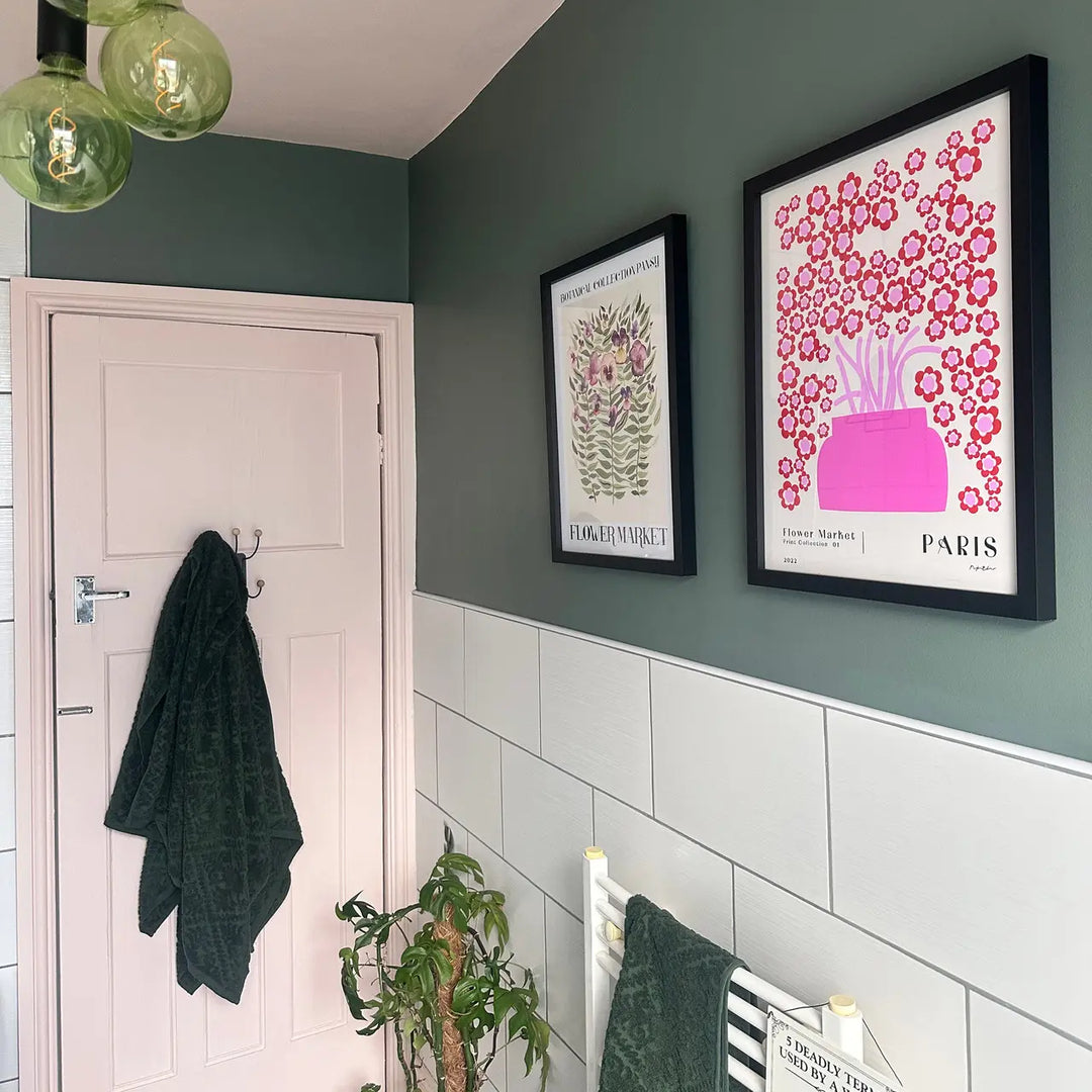Bathroom interior with framed artwork on a green wall, towel hanging on a door, and plant.