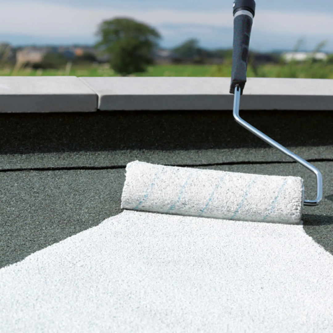 Roller with white paint on a roof surface, with a blurred outdoor background.