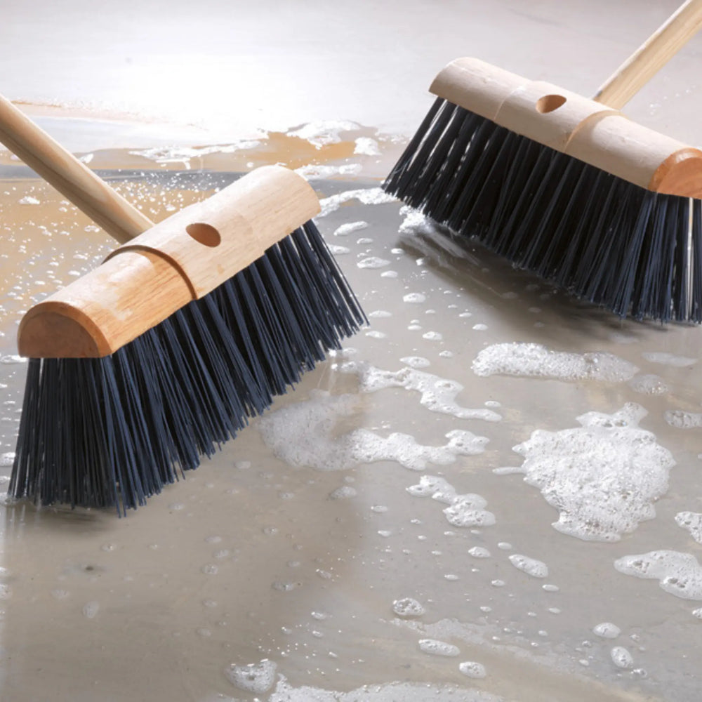 Two brooms with wooden handles and black bristles cleaning a wet floor.