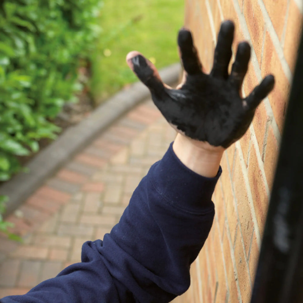 Hand wearing a black glove with paint on it, outdoors.
