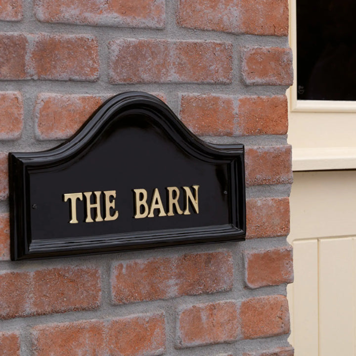 Black sign with 'THE BARN' on a brick wall
