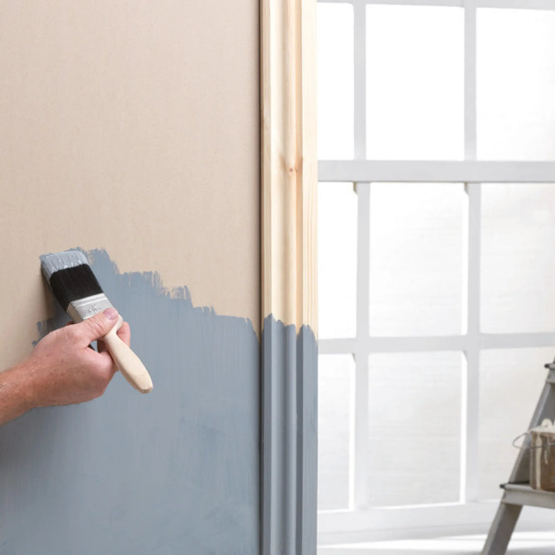 Person painting a wall with a blue paintbrush next to a window.