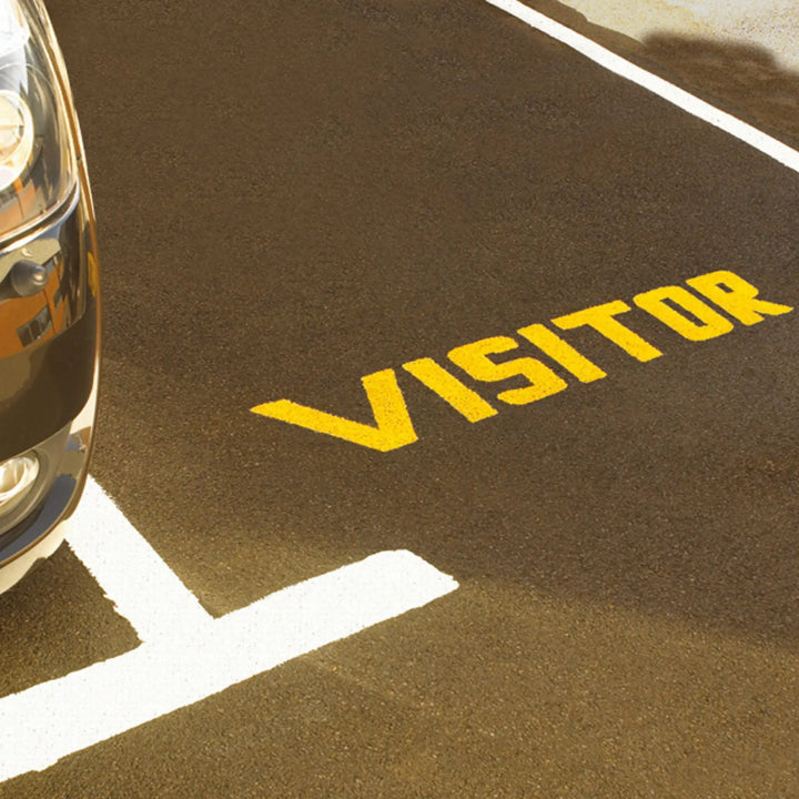 Car parked next to a 'VISITOR' marked space on a brown surface.