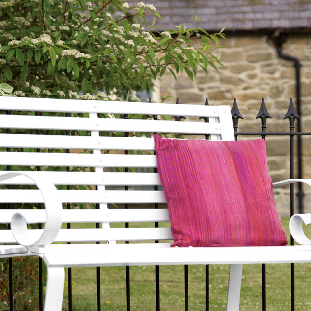 White bench with a pink pillow in a garden setting
