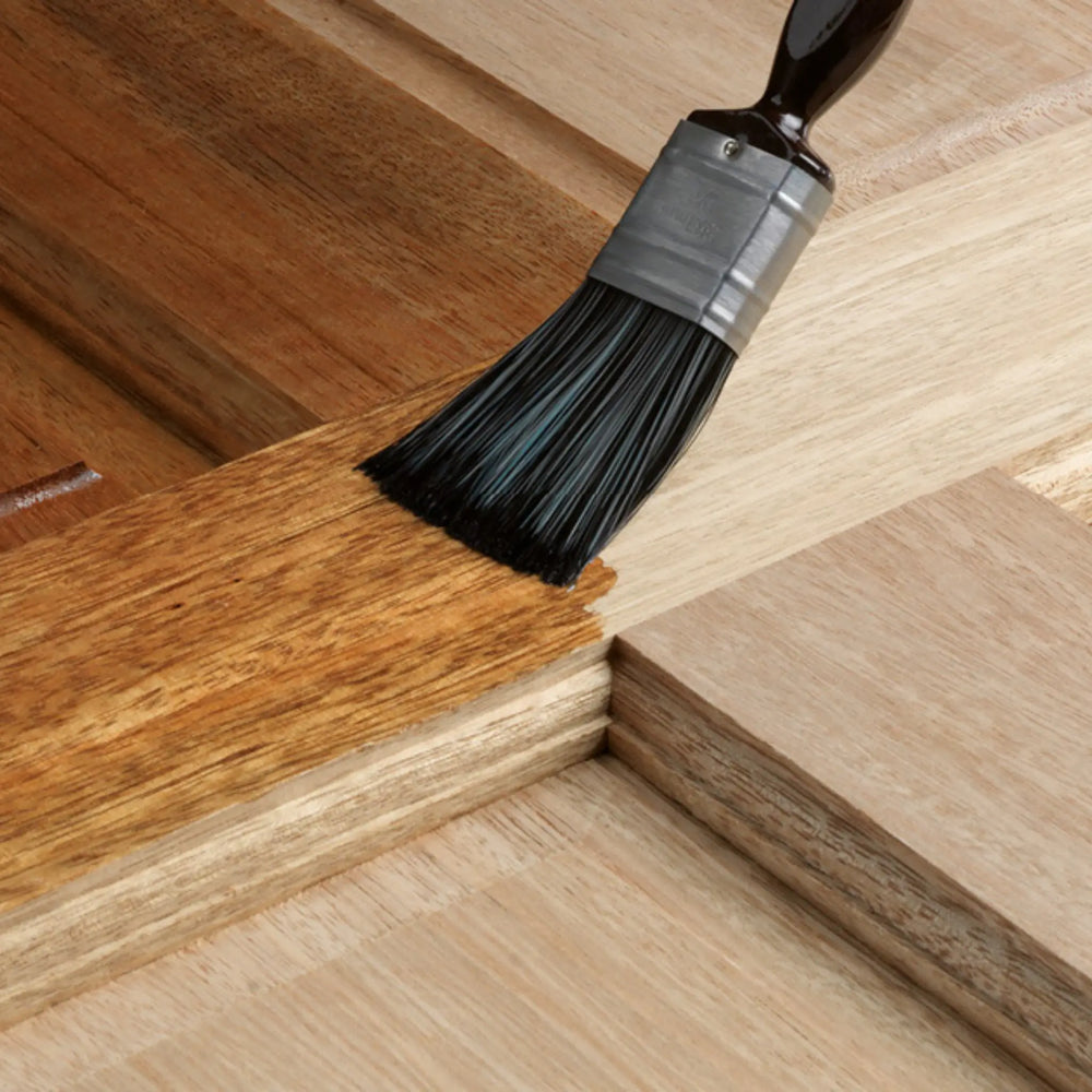 Close-up of a brush applying a finish to wooden flooring
