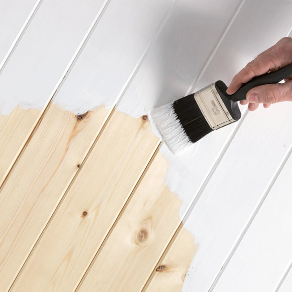 Person painting wooden planks with a brush against a white wall.