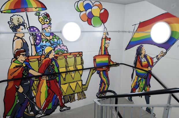 Colorful mural of people with rainbow flags and balloons on a wall.