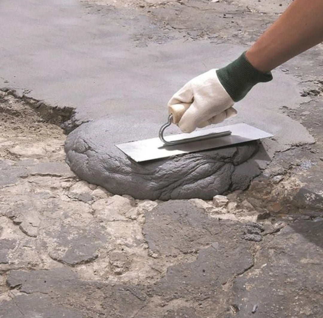 Person applying grey concrex to a repair on a concrete surface using a trowel.