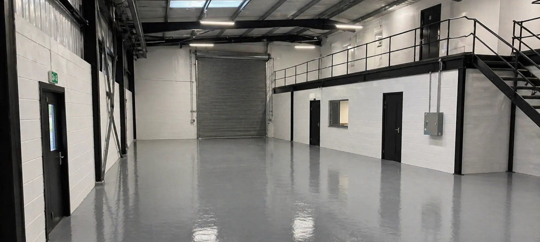Renovated industrial warehouse with white walls, grey concrete floor and metal doors painted in black 