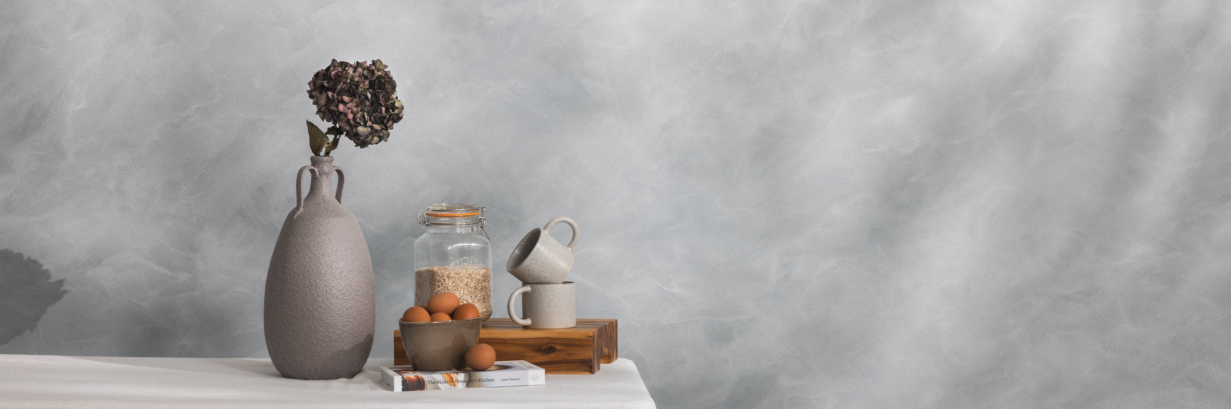 Decorative items including a vase, jar, and small plant on a white surface with a gray background