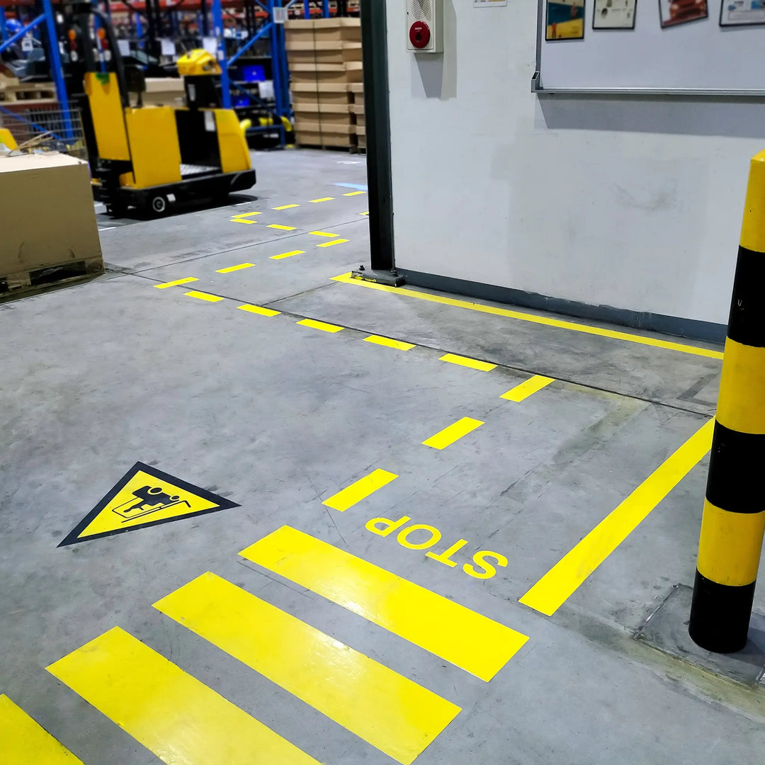 Yellow safety markings on a warehouse floor with a forklift in the background