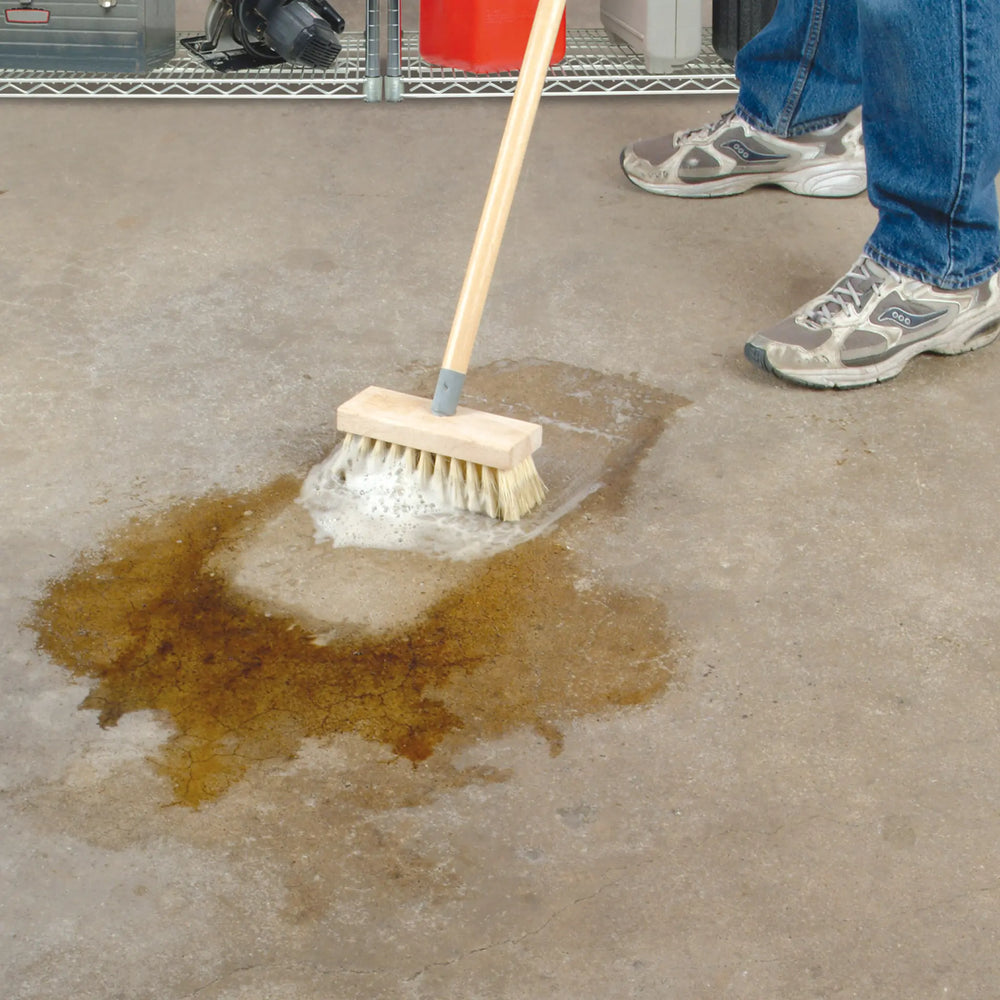 Person cleaning an oil spill on a concrete floor with a brush.
