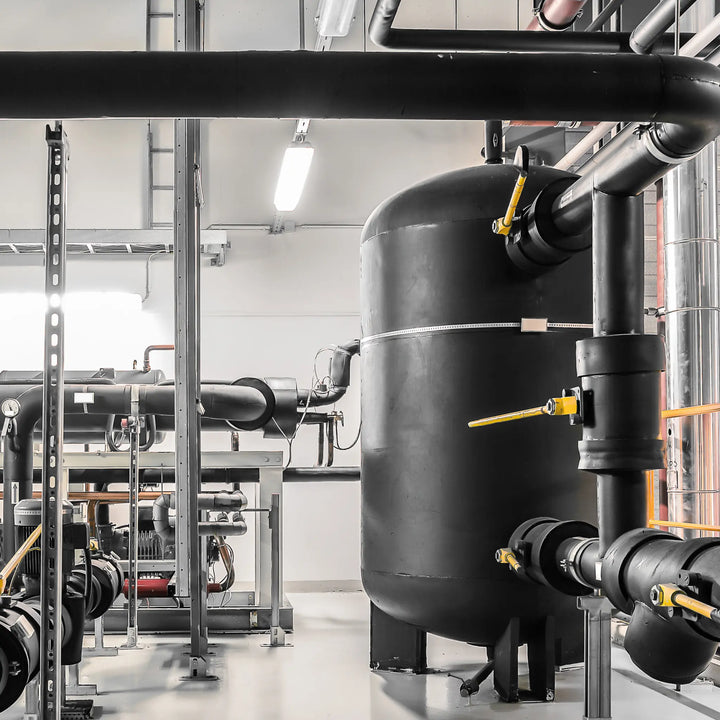 Industrial setting with large black cylindrical tank and pipes in a mechanical room.