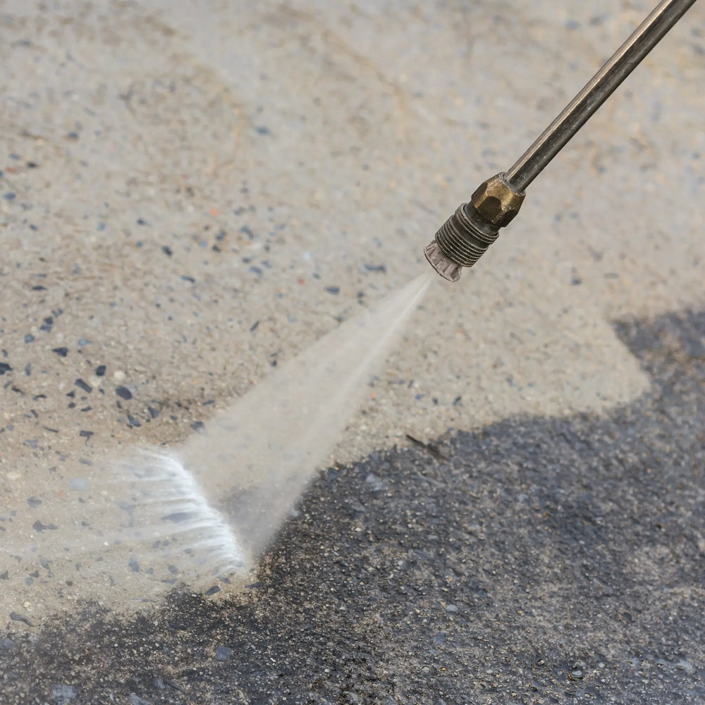 High-pressure water cleaning a concrete surface with a pressure washer nozzle.