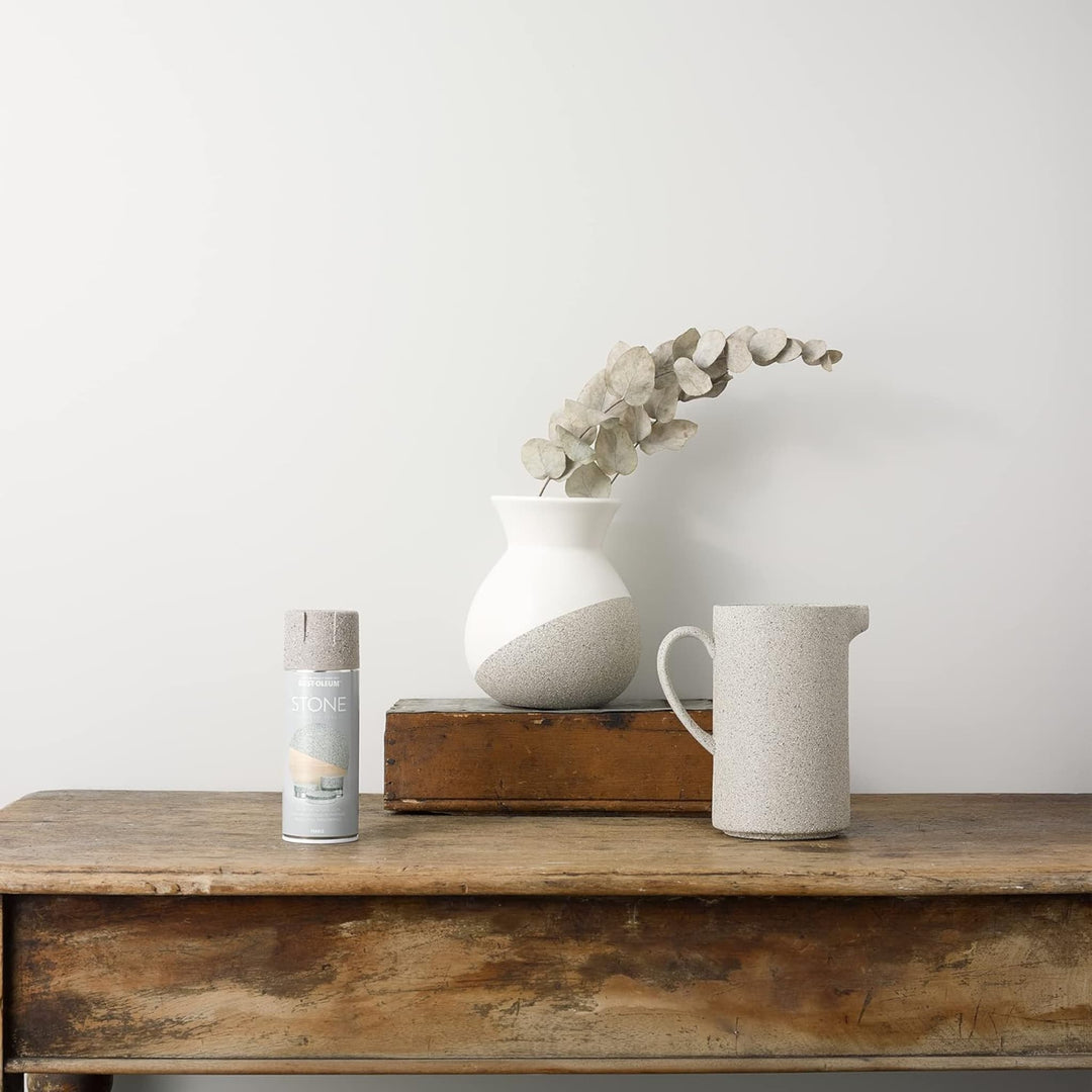 Decorative items including a vase, pitcher, and candle on a wooden surface with a plain background