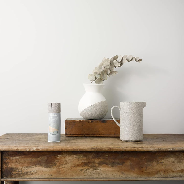 Decorative items including a vase, pitcher, and candle on a wooden surface with a plain background
