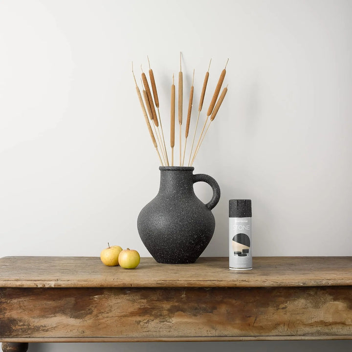 Black speckled vase with dried reeds on a wooden table against a white wall