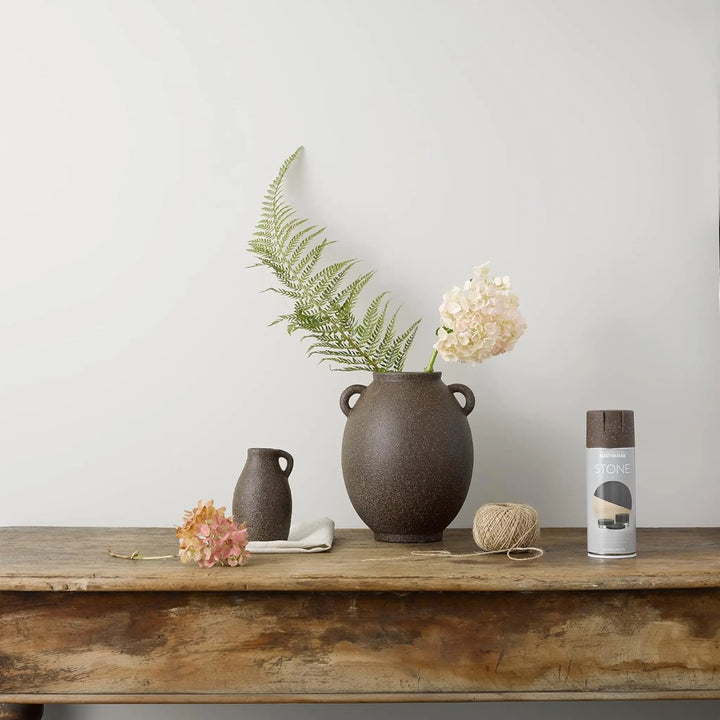 Decorative setup with a brown vase, flowers, and a can on a wooden surface against a light gray background