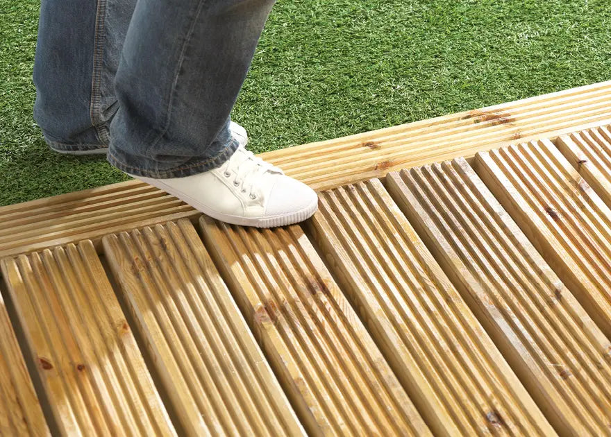 Person wearing white sneakers and blue jeans stepping onto a wooden deck with grass in the background